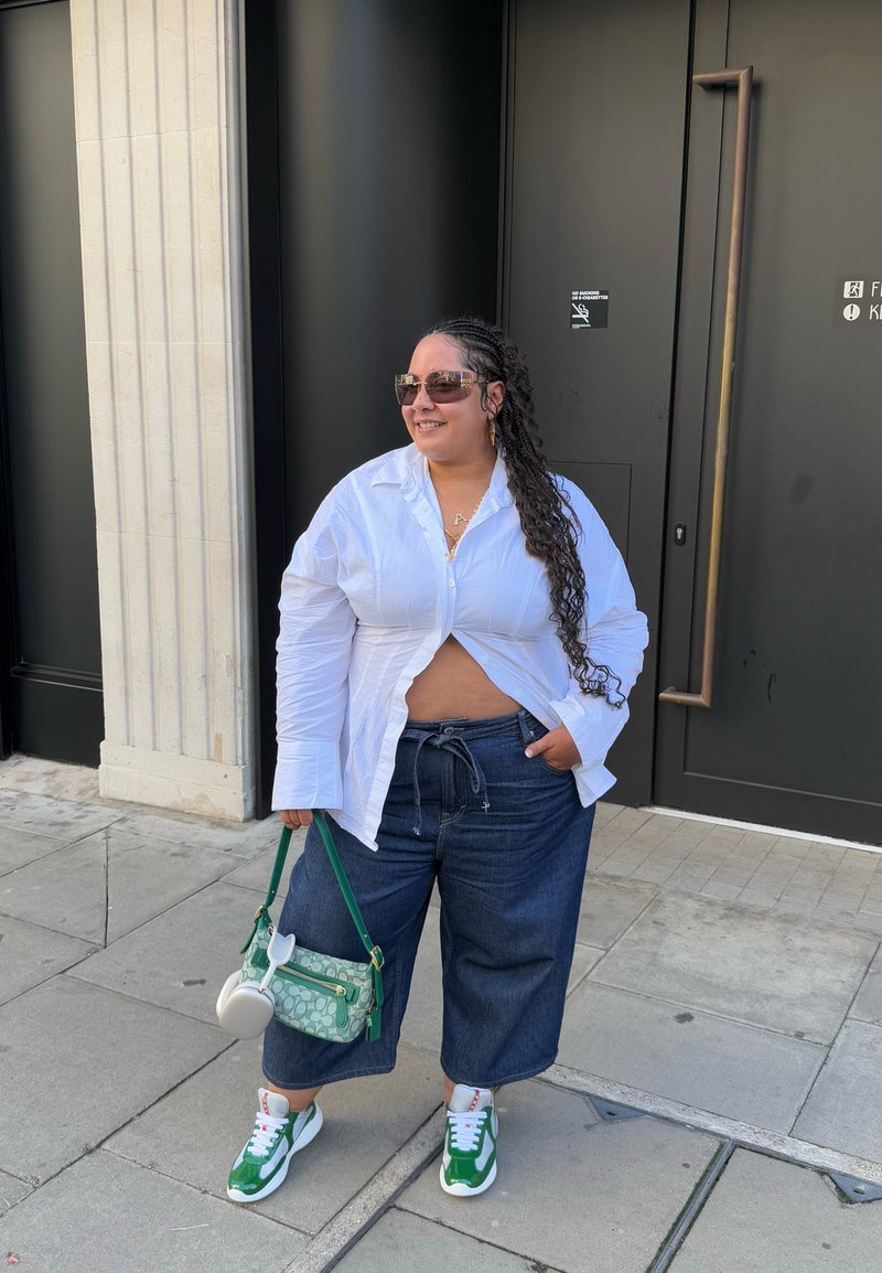 White button-up shirt, dark wide-leg denim pants, green and white sneakers, green handbag, wearing sunglasses, with braided hair.
