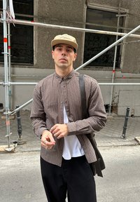 Brūnas un baltas svītrains pogājams krekls pār baltu T-kreklu, kopā ar melnām biksēm un pleca somu. Sudraba gredzeni uz rokām.