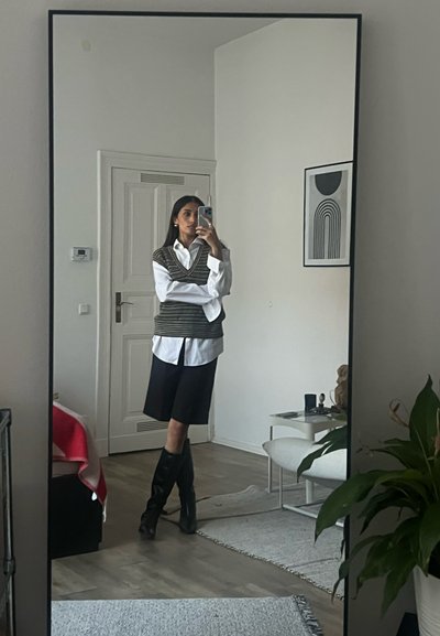 Chaleco de punto a rayas marrón y blanco sobre una camisa blanca, combinado con pantalones cortos oscuros y botas negras hasta la rodilla. Reflejo en un espejo de cuerpo entero.