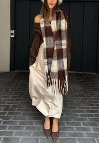 Plaid scarf in brown, cream, and grey woven fabric; soft texture. Brown knitted jumper and cream satin dress; brown heels complete the outfit.