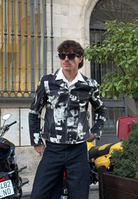 Black and white printed jacket with a collared design, denim texture, and front pockets. Worn with dark jeans, featuring subtle patterns.