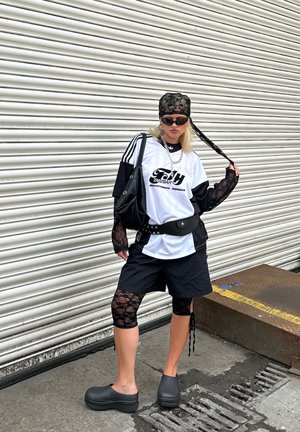 Outfit in black and white featuring a graphic t-shirt, lace sleeves, black shorts, lace knee-length leggings, and black clogs. Accessories include sunglasses and a bag.