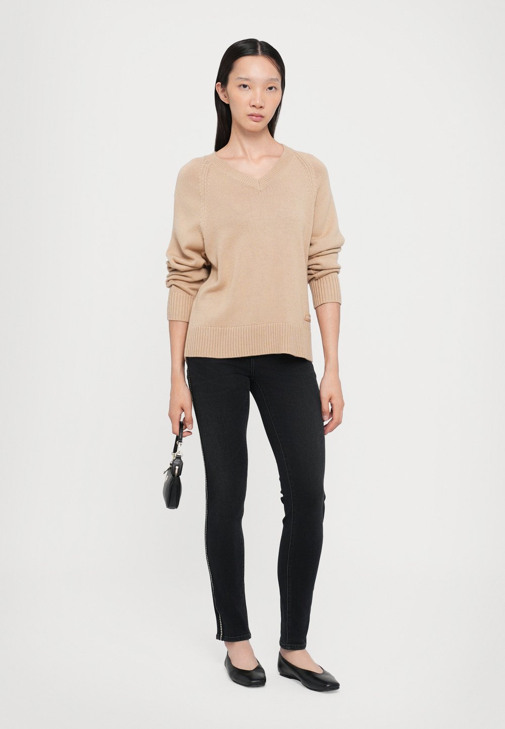 Beige stickad tröja med V-ringning, ribbade ärmslut och nederkant. Kombinerad med svarta smala jeans med sidodetalj. Svarta platta skor.