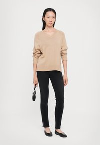 Beige stickad tröja med V-ringning, ribbade ärmslut och nederkant. Kombinerad med svarta smala jeans med sidodetalj. Svarta platta skor.