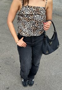 Satijnen top met luipaardprint en dunne bandjes, gecombineerd met zwarte wijde jeans en een zwarte handtas. Zwarte sneakers met witte strepen worden gedragen.