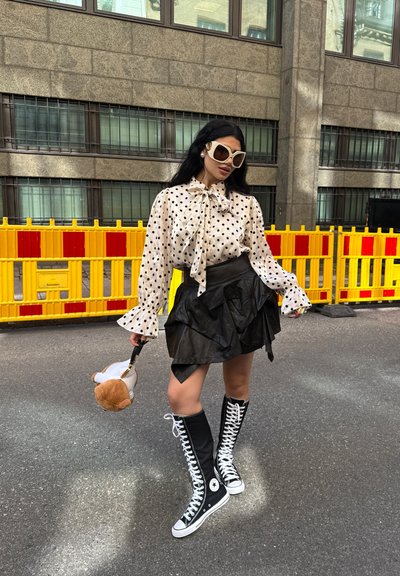 Blusa blanca con lunares negros, lazo, mangas con volantes; mini falda de cuero negra; zapatillas negras hasta la rodilla; sosteniendo un juguete de peluche.