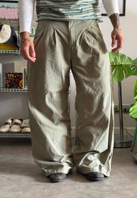 Lichtgroene cargo-broek met wijde pijpen, gemaakt van stevig materiaal, voorzien van voorplooien en een losse pasvorm, gecombineerd met zwarte schoenen.