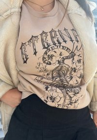 Sweatshirt bej cu un grafic de tigru negru împletit cu desene florale, decolteu rotund și manșete ribbed. Pantaloni negri cu talie înaltă vizibili.