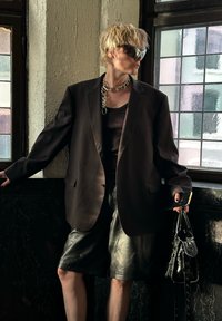 Μαύρο oversized σακάκι πάνω από ένα σκούρο τοπ, σε συνδυασμό με δερμάτινες βερμούδες. Αξεσουάρ περιλαμβάνουν μια χοντρή αλυσίδα στο λαιμό και μια μαύρη τσάντα.