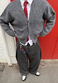 Persona che indossa un cardigan grigio peloso, cravatta rossa, camicia bianca, pantaloni larghi a righe con chiavi e portachiavi di Spider-Man, e scarpe bianche e nere.