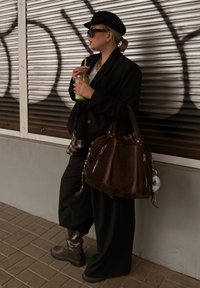 Fekete túlméretezett blézer, alatta kockás ing, fekete bőszárú nadrág, barna bőr kézitáska, sötét csizma, zöld ital és fekete napszemüveg.