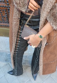 Brown faux fur coat, black leather trousers with lace-up sides, brown patterned handbag, and a gold watch. The shoes are black pointed-toe.