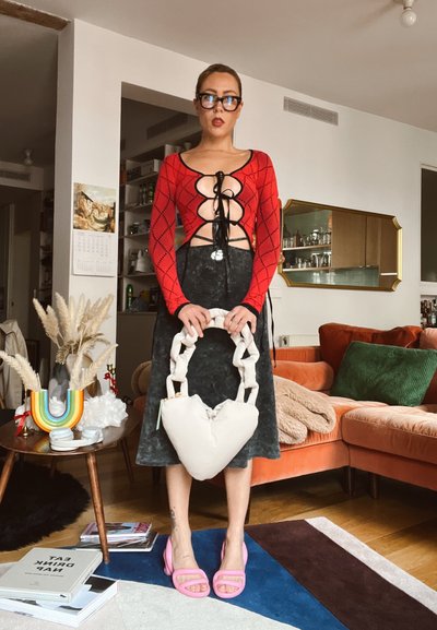 Top rojo de manga larga con cordones en el frente, falda negra, sandalias gruesas rosas y un bolso blanco en forma de corazón con asas de cadena.