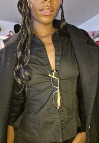 Sort skjorte med knapper og struktureret finish, med dyb V-udskæring. Sølvindfattede briller med orange accenter er stukket ned i skjorten.