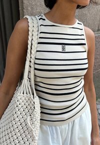 Top sin mangas a rayas en crema y negro, con textura acanalada. Combinado con un bolso tejido blanco texturizado que cuenta con asas trenzadas.