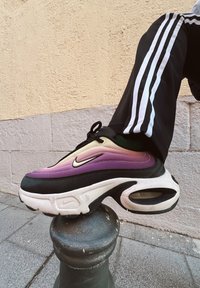 Sneakers Nike z gradientowym wzorem w odcieniach fioletu i kremu, z czarnymi akcentami, masywną białą podeszwą i widoczną poduszką powietrzną.