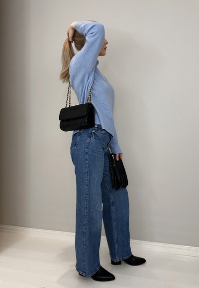Suéter de punto azul claro, jeans azul de pernera ancha, botines negros de tacón y un bolso negro acolchado con una correa de cadena dorada.