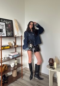 Jeans jakna s svetlo modrimi manšetami, črne plisirane kratke hlače in črne škornje s peto do kolen. Črna torbica z dekorativnimi detajli.