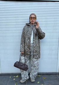 Imperméable à imprimé léopard, pantalon gris à motifs, sac à main marron et chaussures claires. Comprend une capuche et des boutons pression pour la fermeture.