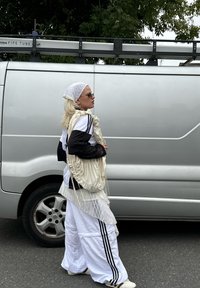 Hvite oversized bukser med svarte striper, en svart og hvit topp, og en lysfarget teksturert veske. Tilbehør inkluderer solbriller og et hodeskjærf.