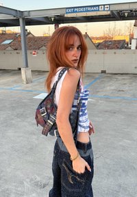 Musta ja monivärinen farkkulaukku hopeisilla metalliosilla ja silmukkadetaljeilla. Malli pukeutunut graafiseen toppiin ja tummansinisiin farkkuihin.