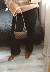 Mörkbrun och krämfärgad randig tröja, svarta byxor med uppvikt fåll och en brun mönstrad clutchväska med guldig kedja. Blanka bruna klackskor.