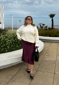 Κρεμ πλεκτό�ς σκούφος με σχέδιο διαμαντιών, μπορντώ σατέν φούστα, μαύρη τσάντα και μαύρα φλατ παπούτσια. Υπαίθριο περιβάλλον με φοίνικες και συννεφιασμένο ουρανό.