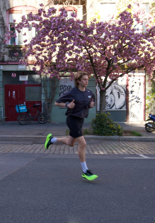 Ung person jogger på gaten med blomstrende rosa kirsebærtre og graffiti-dekte bygninger i bakgrunnen.