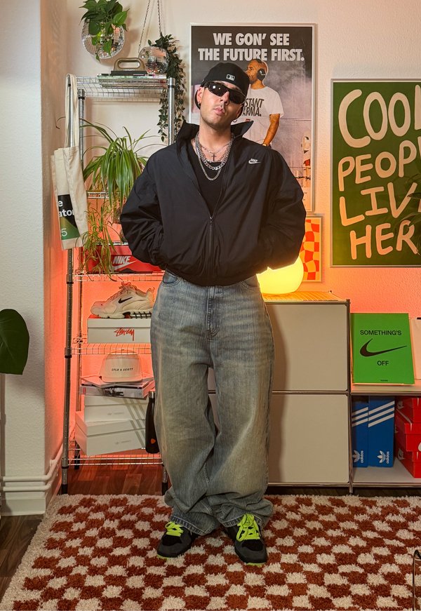 Črni bomberski suknjič, črna majica brez rokavov, svetlo modre ohlapne kavbojke in črni supergi s svetlo zelenimi poudarki. Dodatki vključujejo verižne ogrlice in sončna očala.