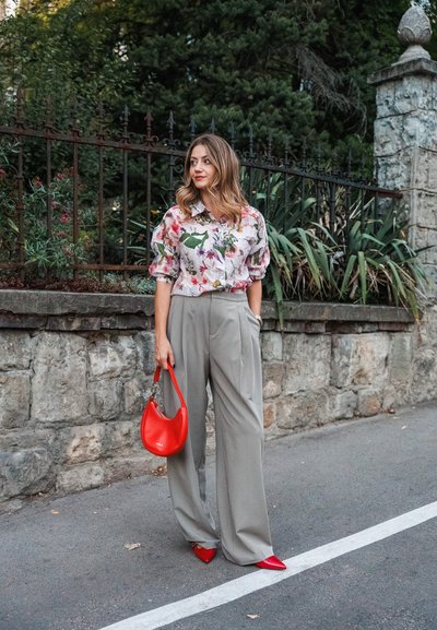Blusa de estampado floral con mangas abullonadas, combinada con pantalones de pierna ancha grises. Los accesorios incluyen un bolso rojo y unos zapatos de punta afilada rojos a juego.