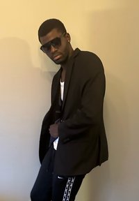 Blazer noir sur un débardeur blanc, porté avec un pantalon de survêtement noir orné d'un motif blanc. De grandes lunettes de soleil noires complètent le look.