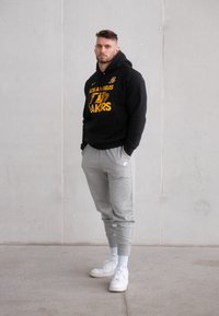 Zwarte hoodie met gele tekst, grijze sweatpants en witte sneakers. De outfit heeft een losse pasvorm en een eenvoudig ontwerp.