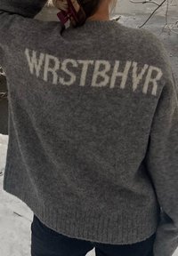 Pull gris à coupe ample, arborant le texte "WRSTBHV" en crème. Confectionné dans un matériau doux et texturé avec un ourlet côtelé.