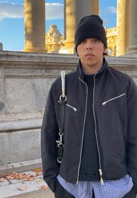 Μαύρο σακάκι με φερμουάρ πάνω από μια υφασμένη μαύρη μπλούζα, στρωμένο με ένα μπλε καρό πουκάμισο. Διαθέτει ιμάντα με διακοσμητικά αξεσουάρ.