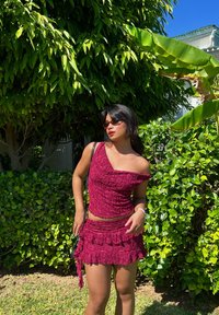 Bordeaux tweed set met een textuur, asymmetrische top en een roezelrok. Geaccentueerd met een kleine crossbody tas en een zonnebril.