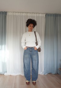 Valge kootud kampsun soonikkoes äärega, sinised kõrge vöökohaga laia säärega teksad, pruun õlakott ja pruunid tossud kollaste paeltega.