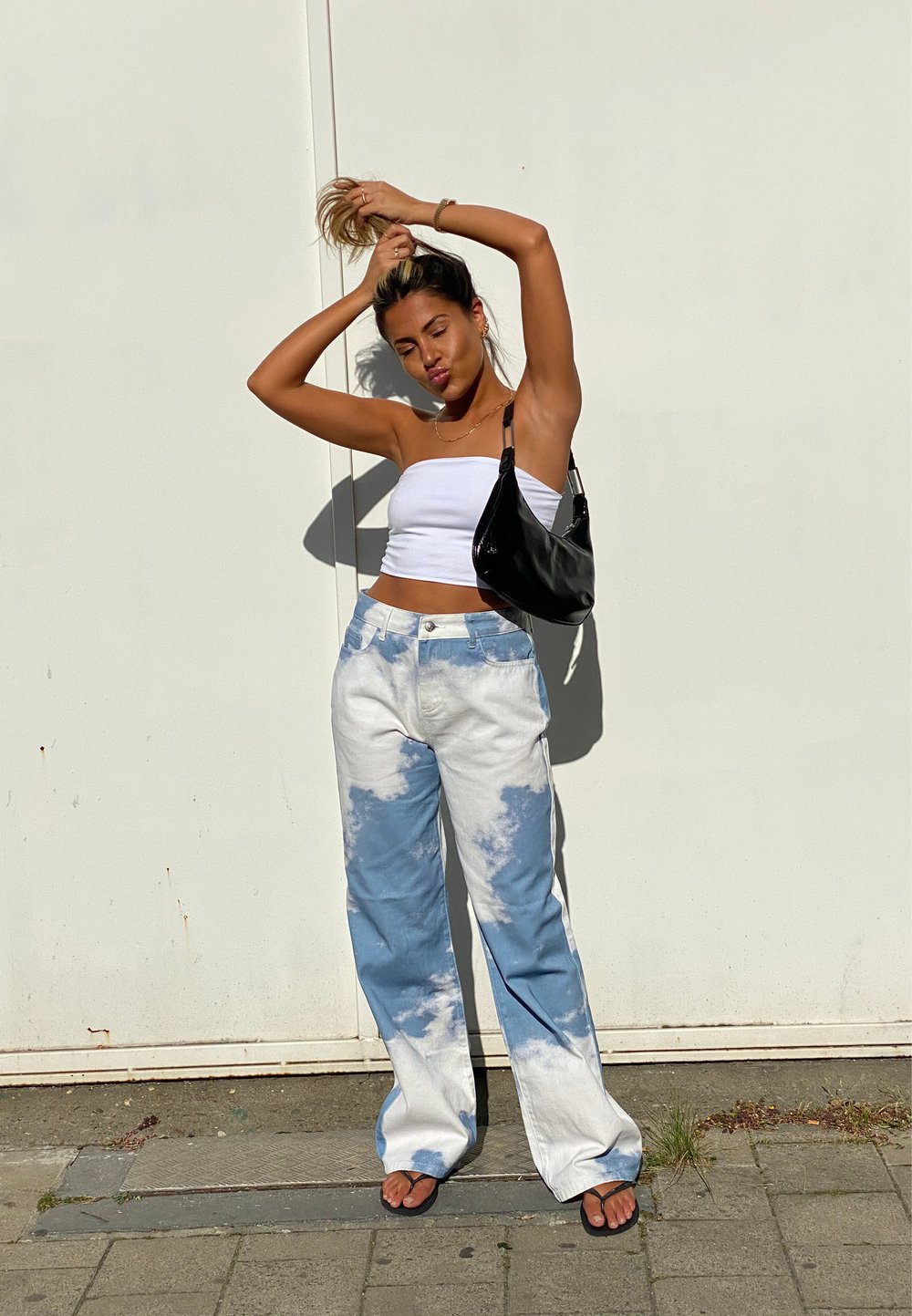 Baggy jeans med et blått og hvitt sky-mønster, kombinert med en hvit crop topp og svart skulderveske. Modellen står p�å et fortau.
