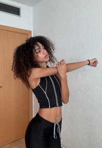 Top curto preto com riscas verticais brancas, combinado com calças pretas com cordão. Cabelo cacheado emoldurado por um fundo claro.