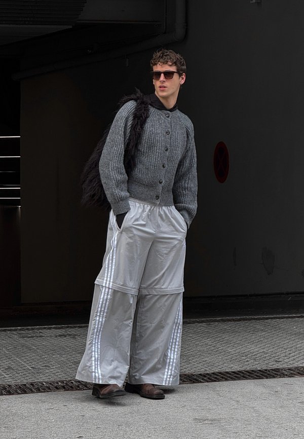 Gray ribbed cardigan with buttons over a black shirt, paired with oversized silver shiny pants with white stripes. Dark sunglasses complete the look.