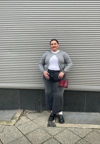 Cardigan gri peste un top alb, asociat cu o fustă lungă din denim negru. Pantofi cu platformă negri și o geantă mică roșie. Fundal texturat.