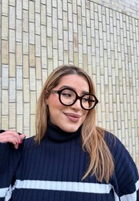 Μαύρα και διαφανή υπερμεγέθη γυαλιά με στρογγυλό σχήμα και παχιά πλαίσια, φορεμένα με έναν ναυτικό ζιβάγκο με λευκές ρίγες.