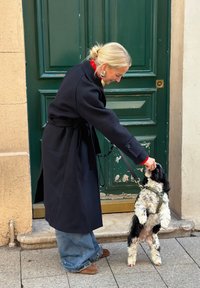 Femme blonde en manteau sombre nourrit un petit chien noir et blanc qui se tient sur ses pattes arrière devant une porte verte.