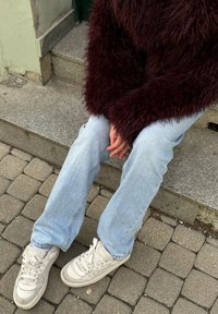 Fuzzy burgundska džemper, svetlo modri ravni traper hlače in krem ​​tenisice s čipkami. Teksturna površina in sproščen kroj, sedeči na kamnitih stopnicah.