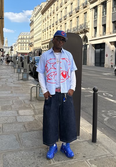 Camisa de rayas azul y blanca de manga corta con un gráfico rojo, camiseta de manga larga blanca debajo, culottes de mezclilla y zapatillas azules.