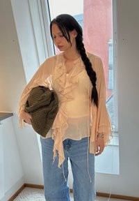 Šviesiai persikinė, permatoma palaidinė su raukšlėmis, ilgomis rankovėmis; derinama su mėlynomis džinsinėmis kelnėmis ir tekstūruota alyvuogių žalios spalvos rankine. Minimalūs aksesuarai.