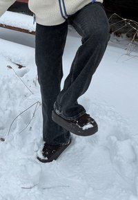 Chaussures marron à enfiler avec une tige texturée, un bout arrondi et des semelles épaisses en caoutchouc, partiellement couvertes de neige, portées avec un jean foncé.