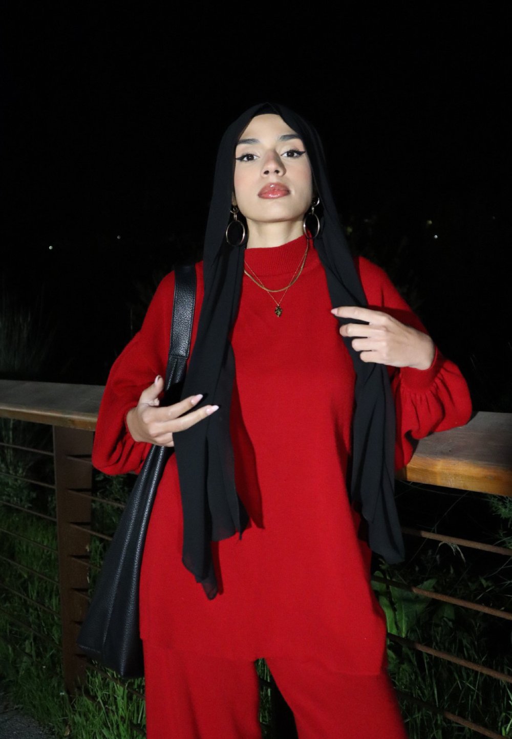 Piros, oversize pulóver hosszú ujjakkal és bordázott textúrával, fekete hidzsbával párosítva. Nagy fülbevalók és rétegezett nyakláncok fokozzák a megjelenést.