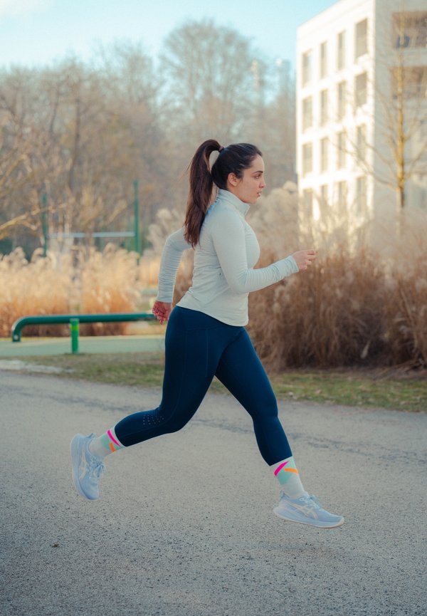 Femme en tenue de sport courant sur un chemin pavé avec des arbres et un bâtiment en arrière-plan pendant la journée.