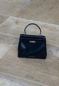 Geantă din piele neagră cu formă structurată, mâner scurt, buzunar frontal și accente din metal auriu. Logo gravat pe partea frontală.