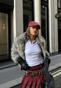 Műszőrme kabát szürke árnyalatokkal, fehér trikó, piros kockás szoknya, fekete kesztyűk, piros kockás sapka, ezüst láncos öv kulcsokkal, fekete steppelt kézitáska.